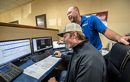 Student sitting at a computer, sharing a laugh with instructor