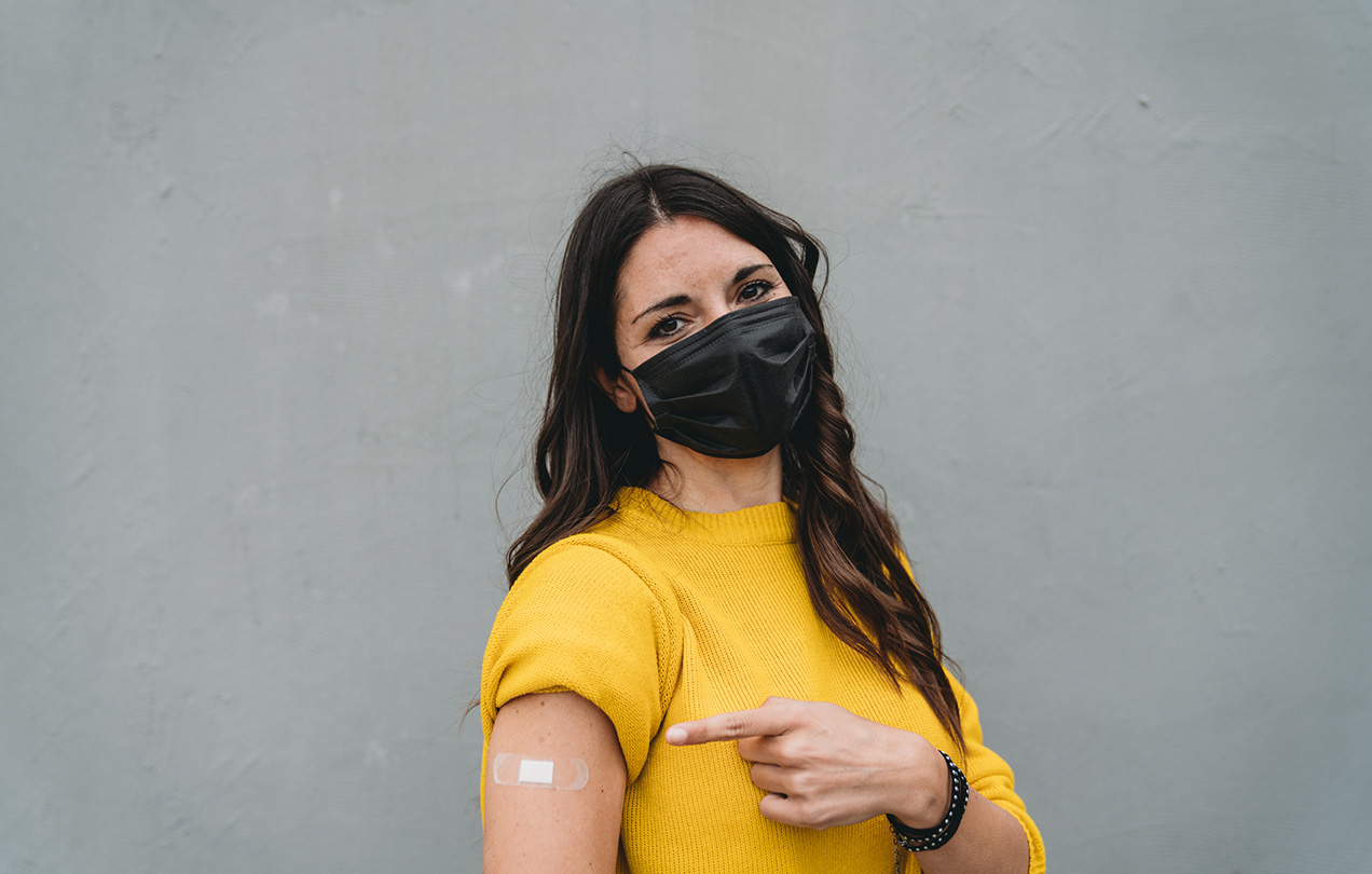 A person pointing to the bandaid from their vaccine