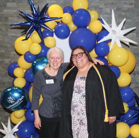 A student and a faculty member posing for a picture in front of an arch of balloons