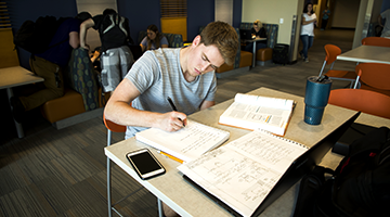 Student studying at a table with papers spread around
