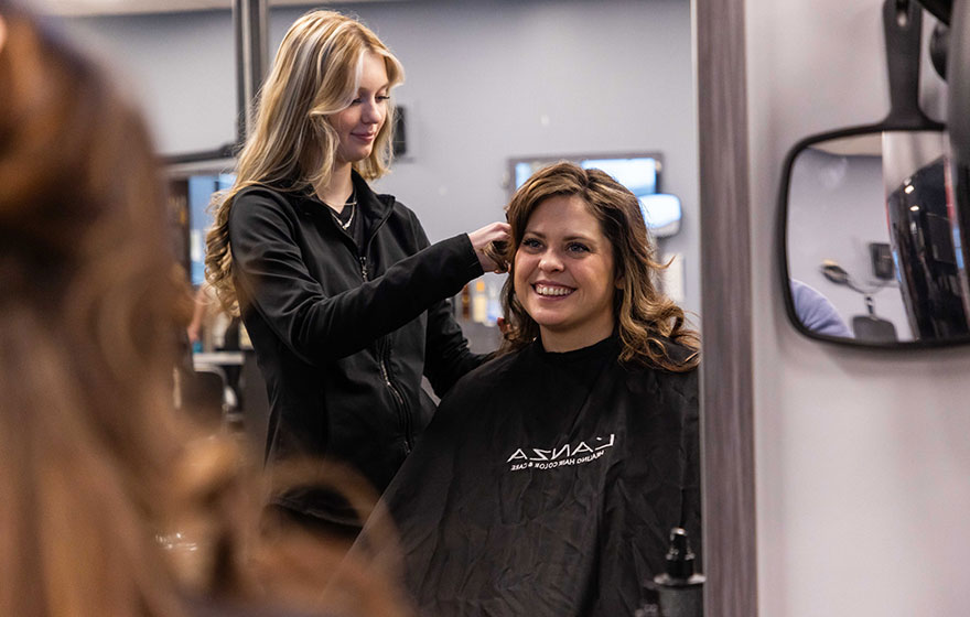 Student styling hair on a client in a salon setting.