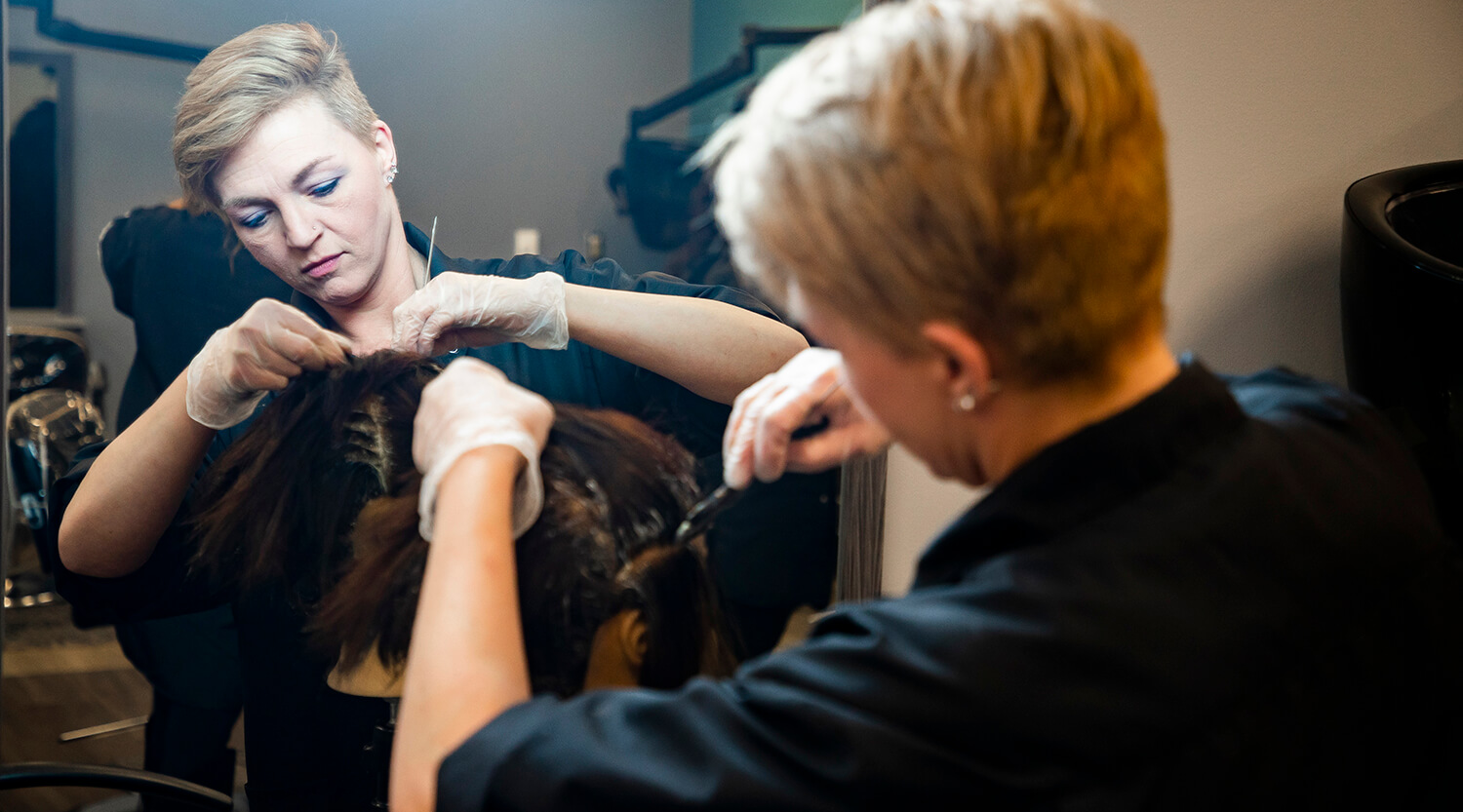A cosmetology student working on hair color with a mannequin