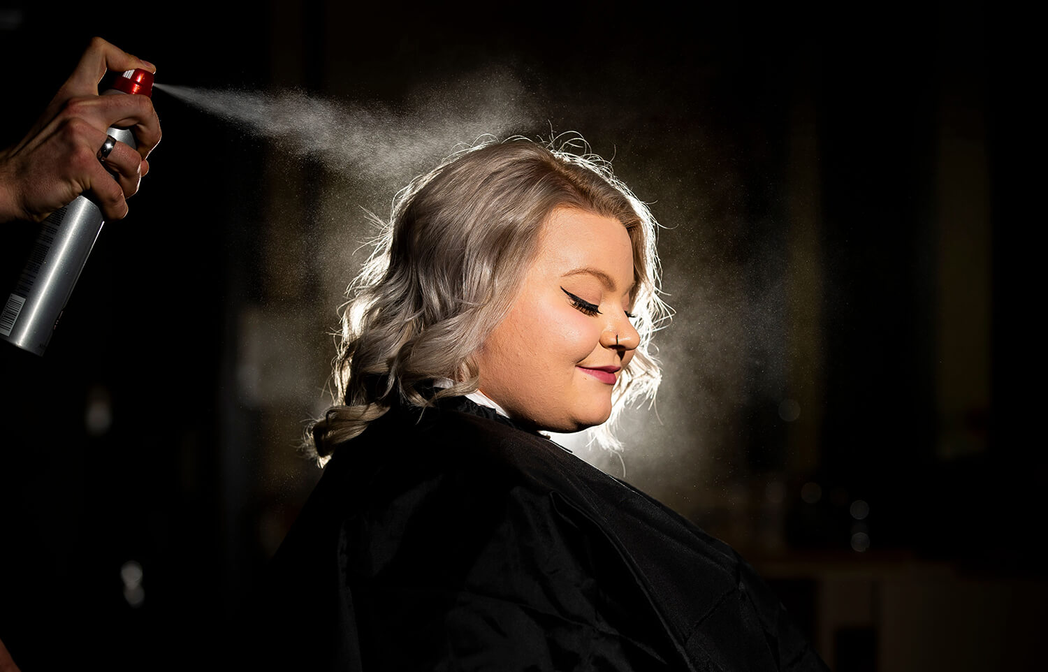 A cosmetology client having their hair sprayed