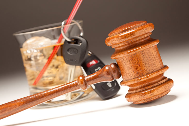 A set of car keys and a glass filled with an alcoholic beverage in the background with a judge's gavel in front