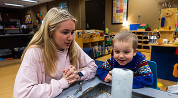 An Early Childhood Education student and a kid creating a science experiment in a drinking glass