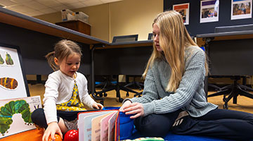 An Early Childhood Education student reading to a toddler-aged kid