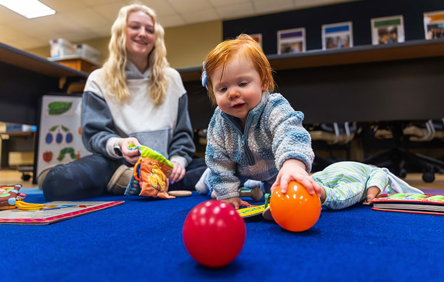 A toddler playing with pit balls in classroom with student