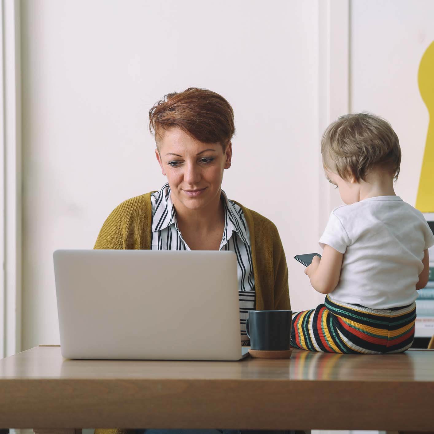 A parent attending an online while class with a toddler sitting nearby