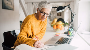 Older woman working on laptop and taking notes