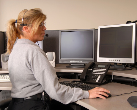 An emergency dispatcher sitting in front of multiple computer monitors and wearing a headset on