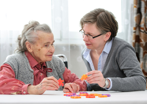 An aging adult playing a jigsaw puzzle a caregiver
