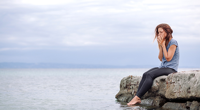 A person sitting on a rock at a lake in a contemplative state