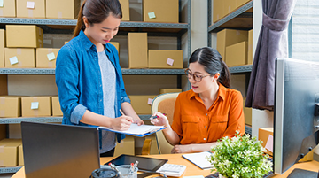 A business leader sitting at a desk and an employee showing her a document