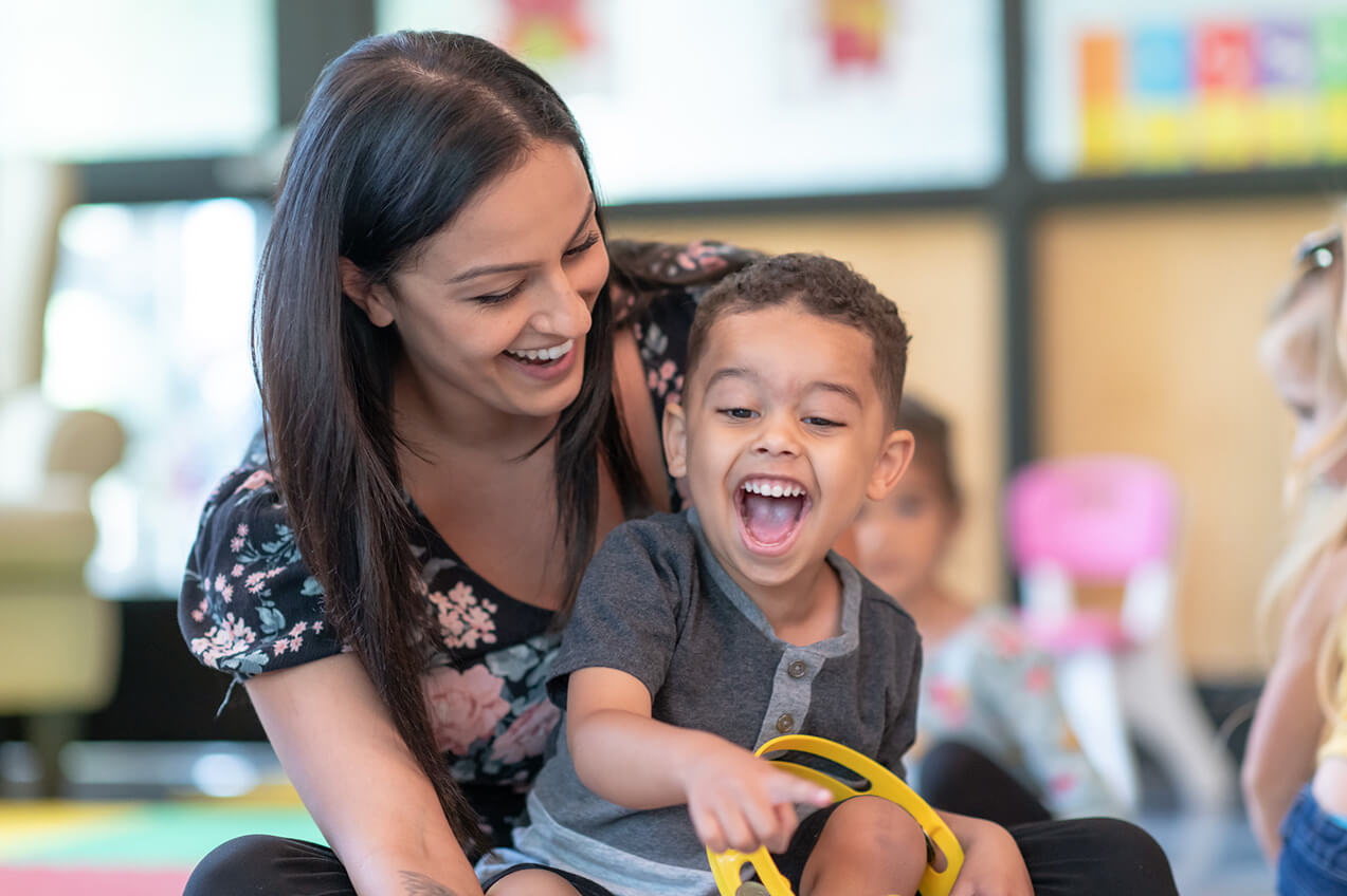 A group child care worker laughing with a preschool-aged kid