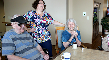A healthcare caregiver laughing with residents of a community-based residential faciity