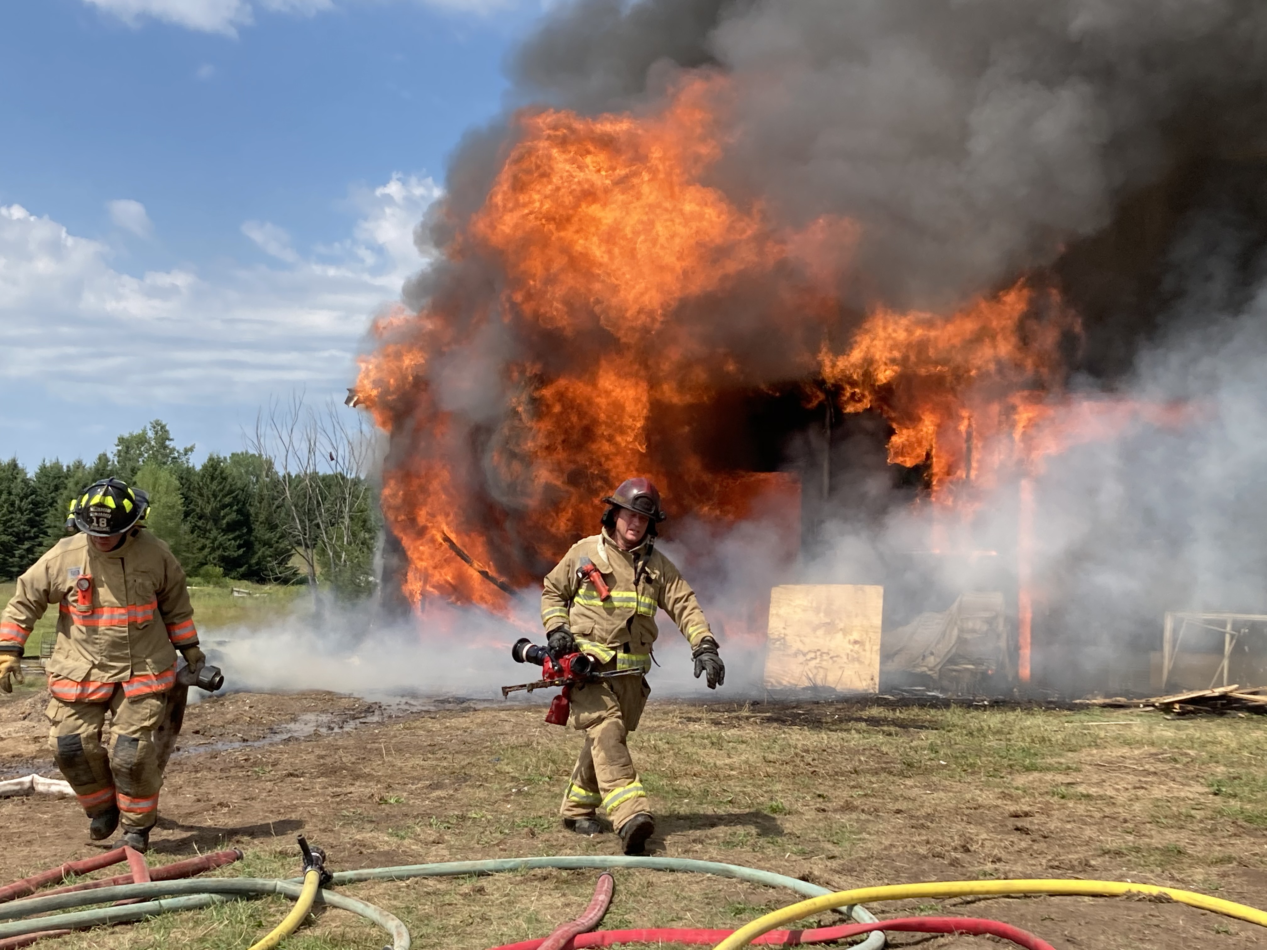 Fire training Firemen in full gear practice with house on fire in background