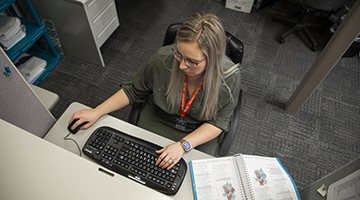 A medical administrative professional looking at a computer with a textbook nearby