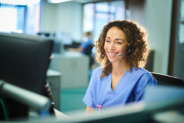 Medical billing professional wearing scrubs and a headset, working at a computer in an office setting.