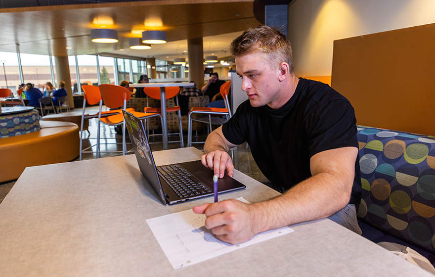 A person sitting in a booth studying with books and a laptop