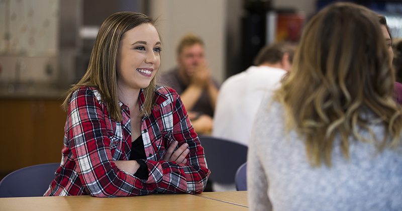 Student smiling at a table while listening to friends in Rice Lake