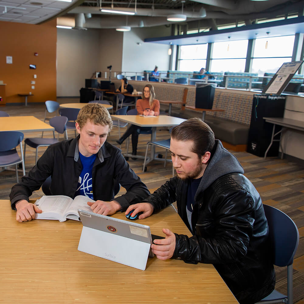 Two students sitting in the Hub and looking at a tablet