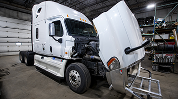 A semi truck with its hood open in the shop