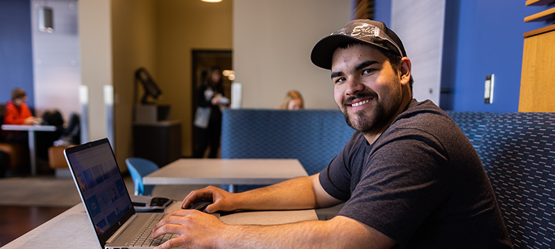 Student smiling at camera and working on laptop