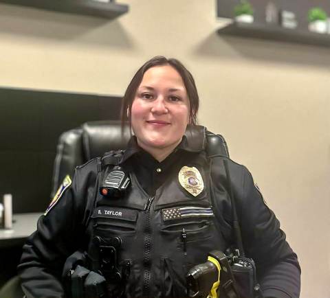 Susie Taylor, wearing her police uniform and seated at her desk, smiles toward the camera.