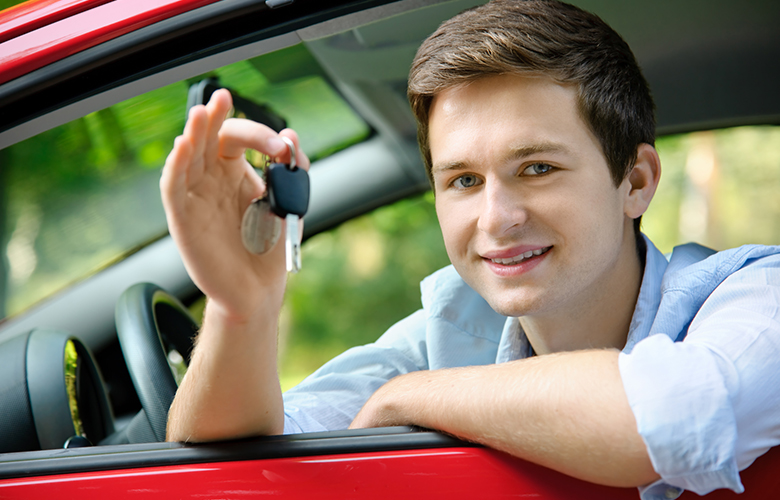 Happy teenage boy holding car keys as he leans out driver's side window of a car.
