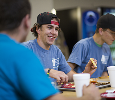 Young man wearing a WITC shirt eats lunch with other students.