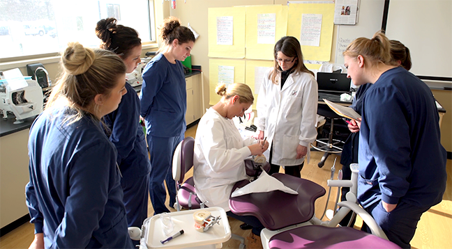 Dental students gathered around an instructor doing a demonstration