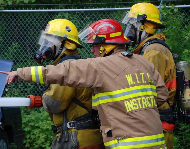 Fire training Firemen in full gear practice with fire hose as instructor points and gives direction.