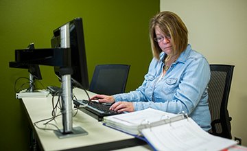 A student reading from a textbook while working on a computer