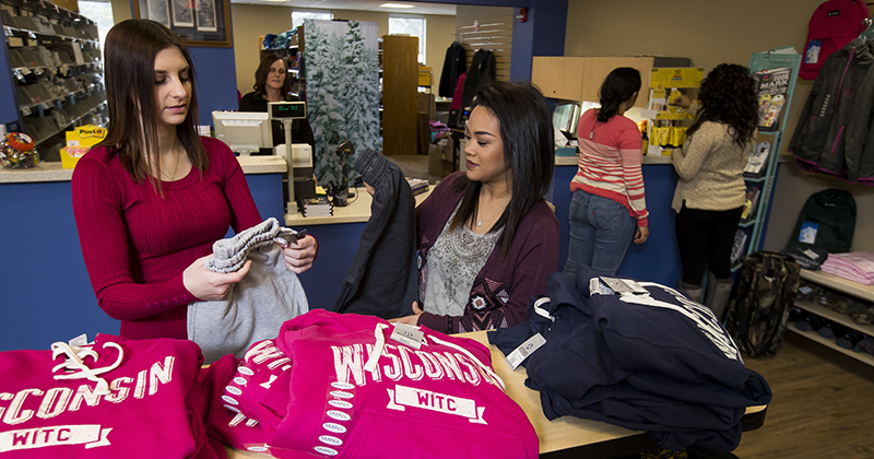 Two female students in the book store sift through WITC shirts and sweatshirts