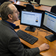 Middle-aged man in glasses works on a computer with two screens in a business classroom.