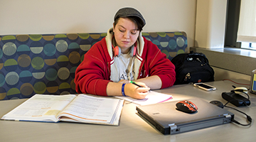 Student studying in a booth with papers and a laptop