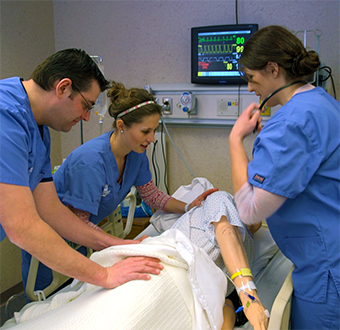 Three nursing student work with a simulation man and turn the body over on a hospital bed