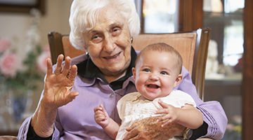 An aging adult sitting in a rocking chair and holding a baby