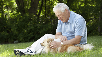 An aging adult sitting outside and petting a dog