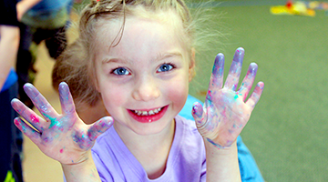 Child smiling and holding up messy and sparkly hands