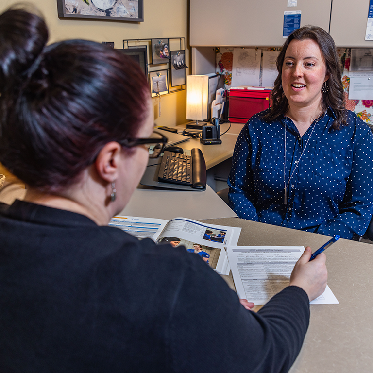 A staff member sitting at a desk with a student to provide information and assistance. 