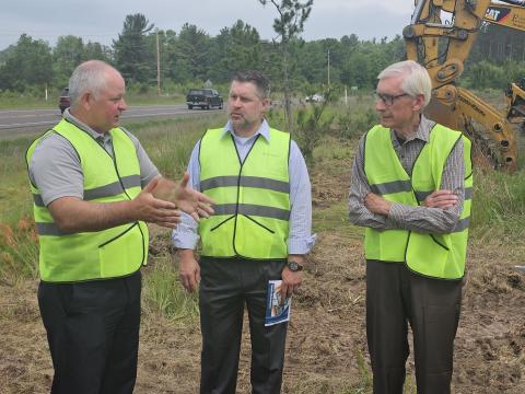 John Will, Brett Gerber, and Gov. Evers stood outside in safety vests reviewing Trailview Cottages site plans in Hayward, WI.
