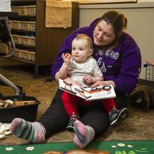 A student teacher holding a toddler and reading a book