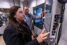 A student using a CNC machine as an instructor watches