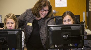 An instructor assisting two students at their computers