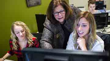 Student at computer with instructor watching over her shoulder and helping her