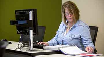 Student sitting at a computer, reading from a book
