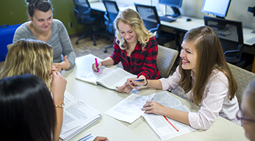 A group of students gathered around at a table and laughing while studying