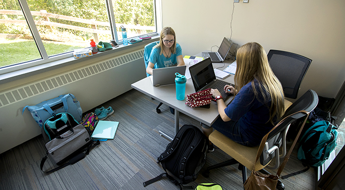 Two students studying at a table together with their laptops