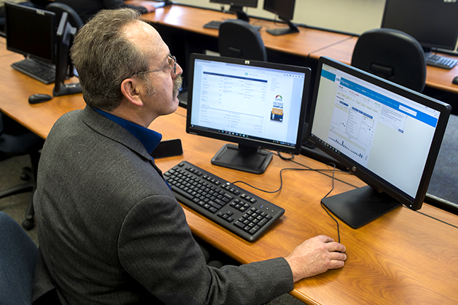 Financial Services student wearing a suit and sitting and analyzing stocks on a computer